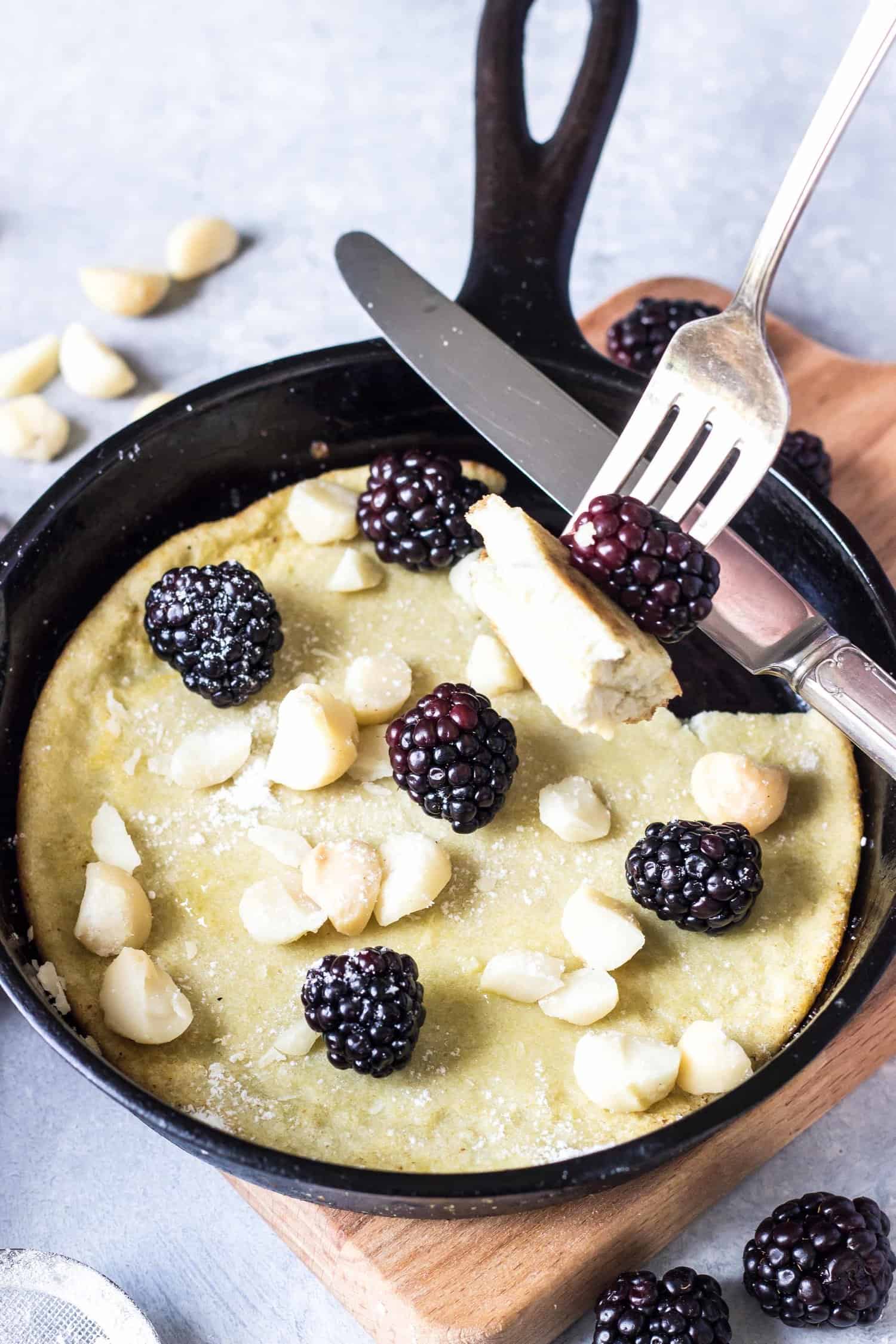 Keto Dutch Baby in a small cast iron skillet topped with blackberries and macadamia nuts.