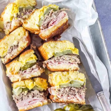 Keto Cuban Sliders in a tray with white parchment paper, pickles and mustard on the side