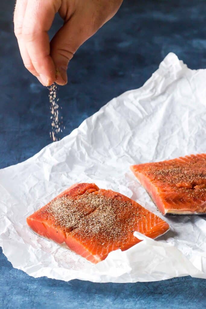 salmon fillets on parchment paper being seasoned