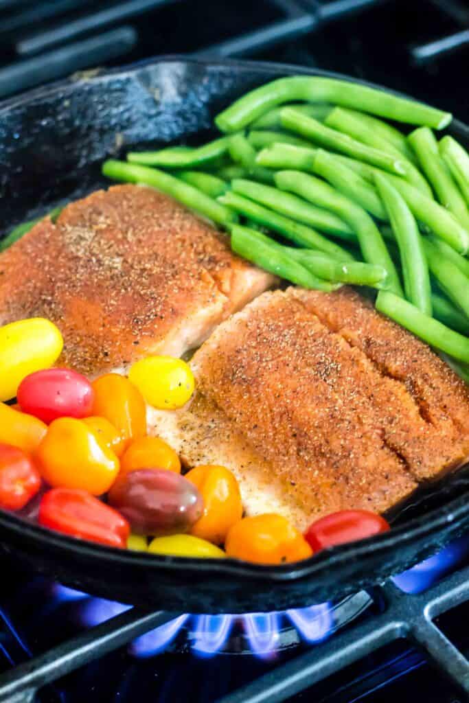 salmon with burst tomatoes and green beans in skillet on stovetop