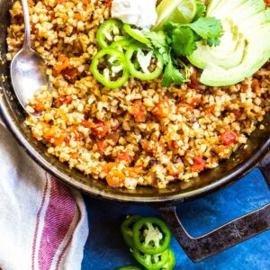 Mexican Cauliflower Rice in a cast iron skillet topped with sour cream, cilantro, avocado, and jalapenos