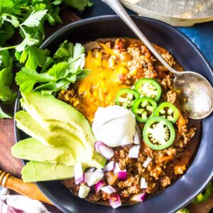 Keto Chili in a bowl topped with avocado, sour cream, sliced jalapeños, and cheese