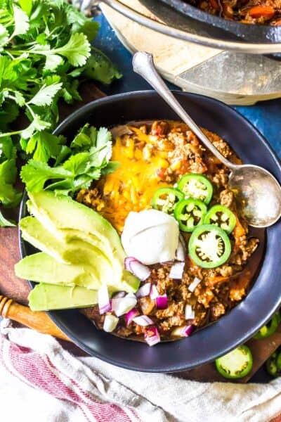 Keto Chili in a bowl topped with avocado, sour cream, sliced jalapeños, and cheese