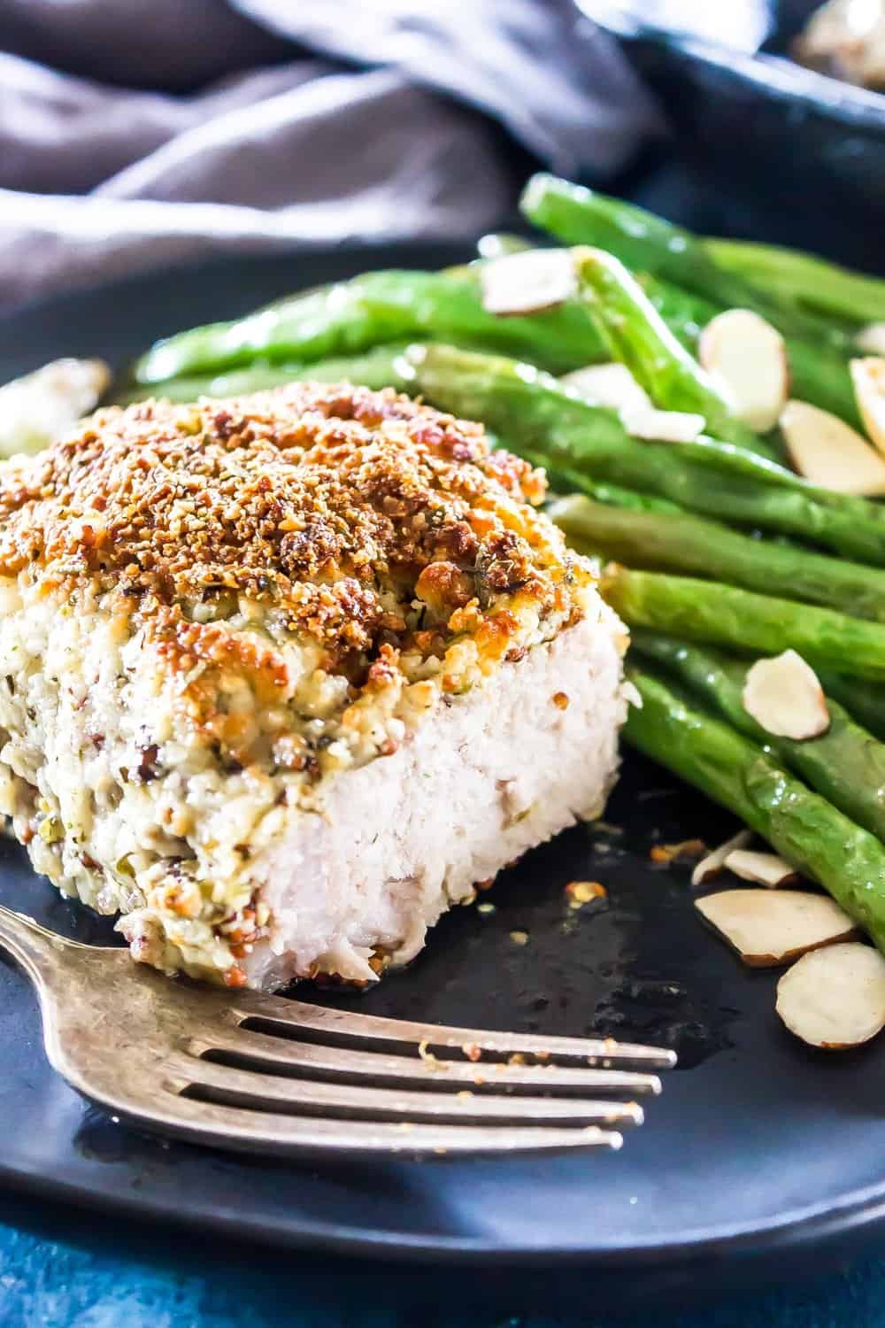 Close up of Keto Parmesan Crusted Pork Chops sliced on a plate with green beans in the background