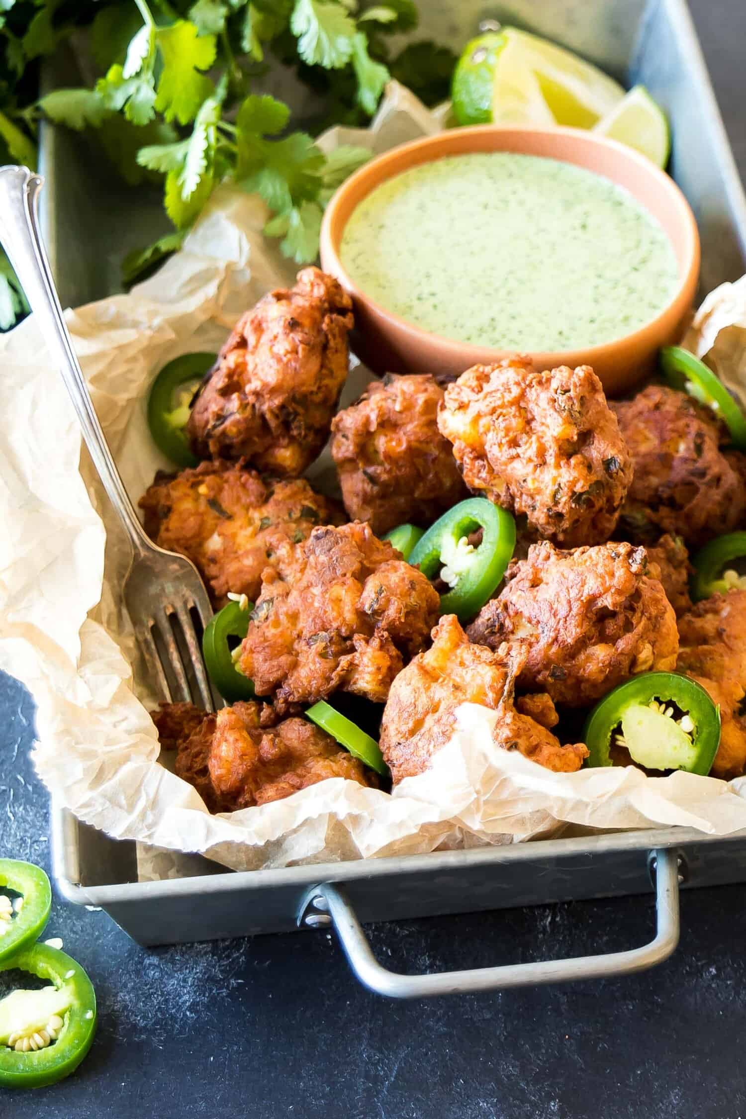 Hushpuppies in a tray, with a bowl jalapeno sauce directly behind