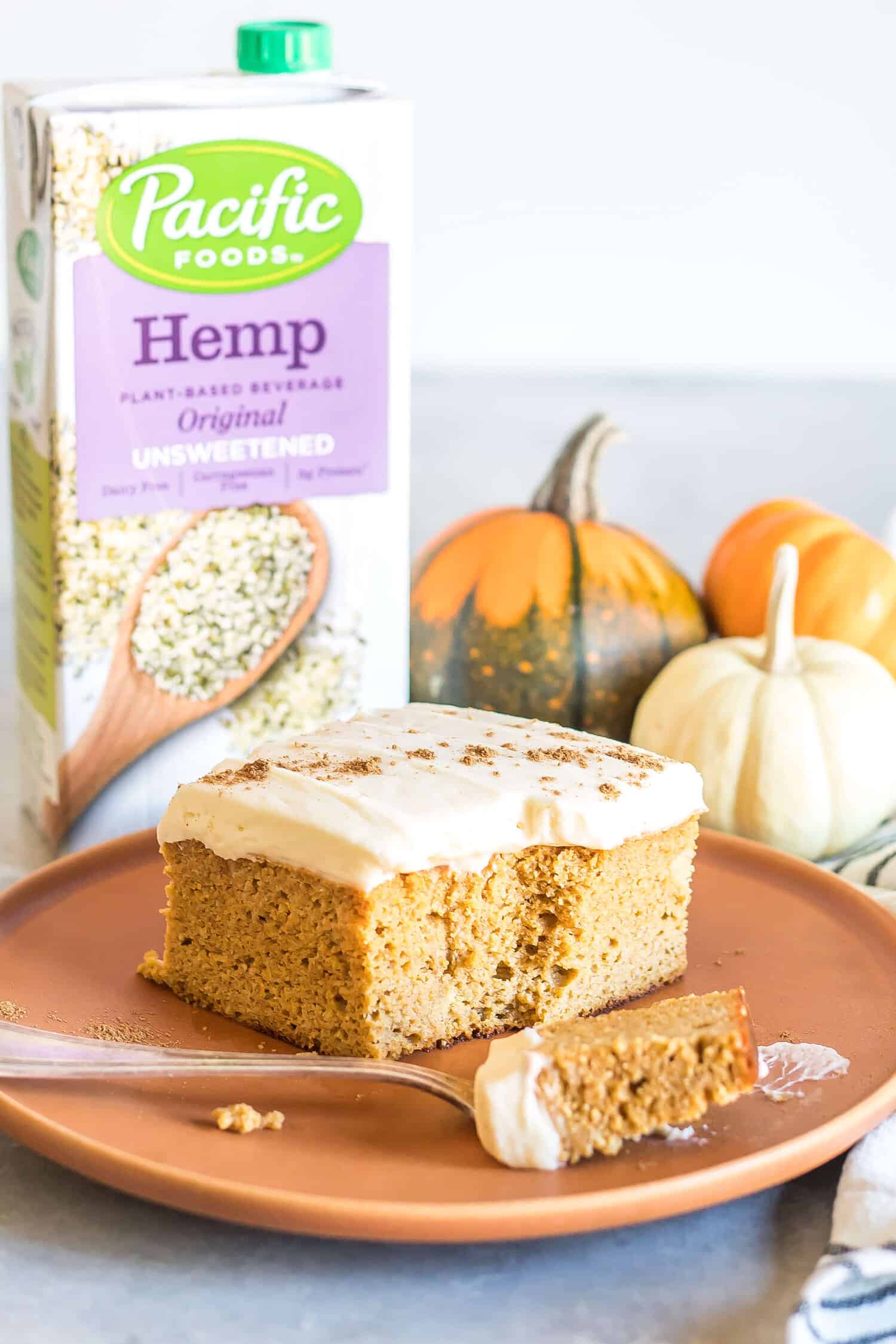 A slice of keto pumpkin spice cake on a plate in front of a carton of pacific foods unsweetened hemp beverage.