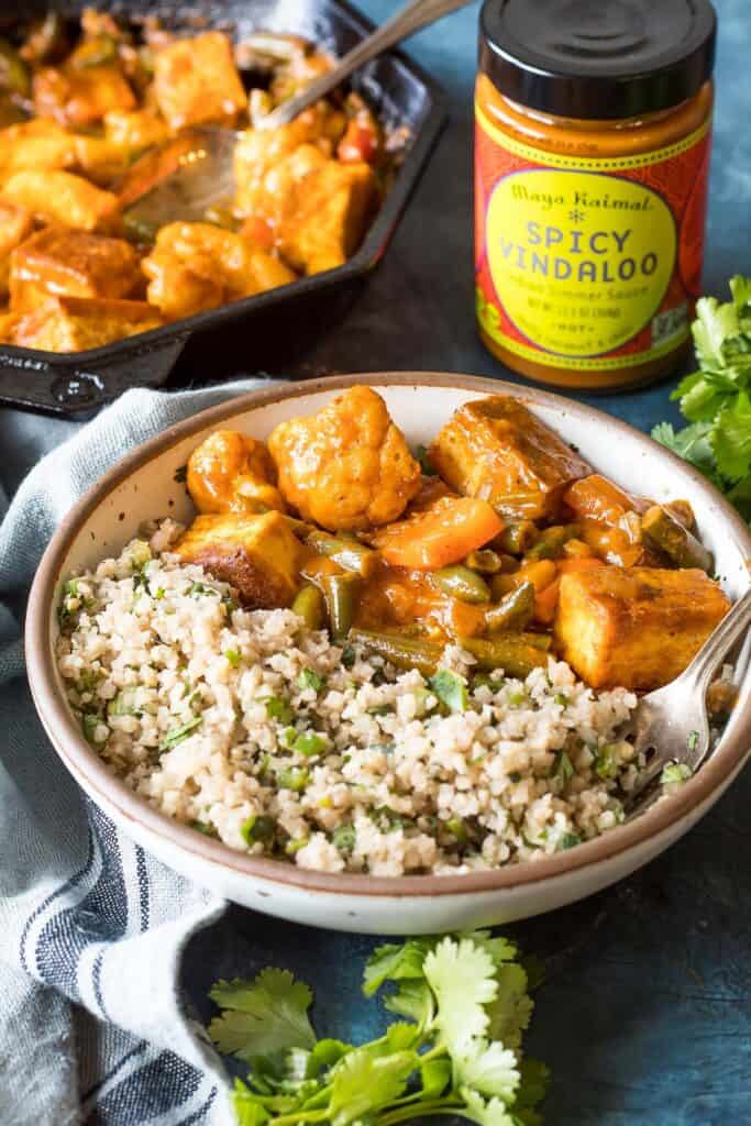 keto vegan tofu vindaloo in a bowl, skillet with leftovers and a bottle of vindaloo simmer sauce in the background