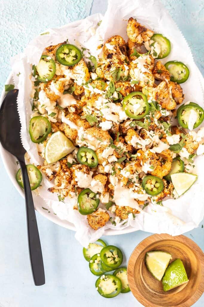 Keto Street Style Cauliflower on a plate lined with white parchment paper, there's a bowl of cut limes and sliced jalapenos