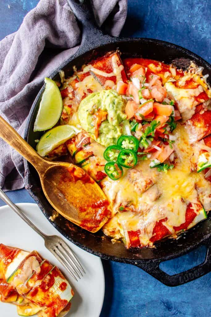 Keto Enchiladas [with Zucchini Tortillas] in a cast iron skillet topped with pico de gallo, guacamole, and jalapenos