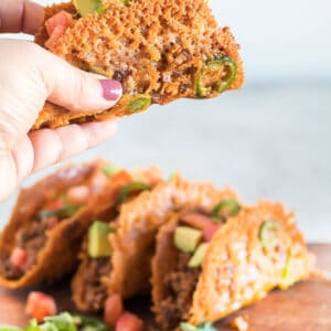a single taco being held close to the camera. Other tacos on a serving board in the background