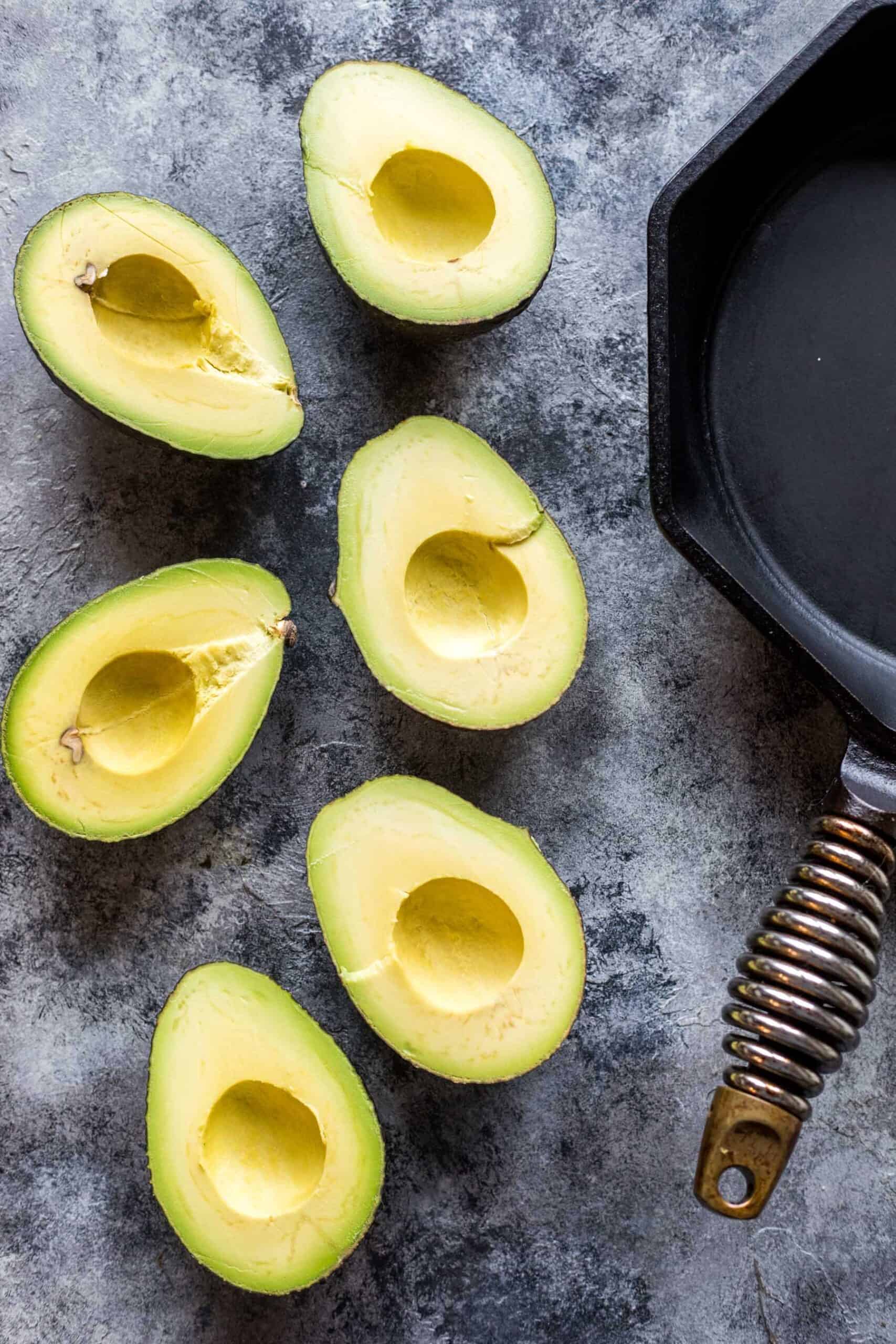 6 avocado halves and a cast iron skillet on a gray background