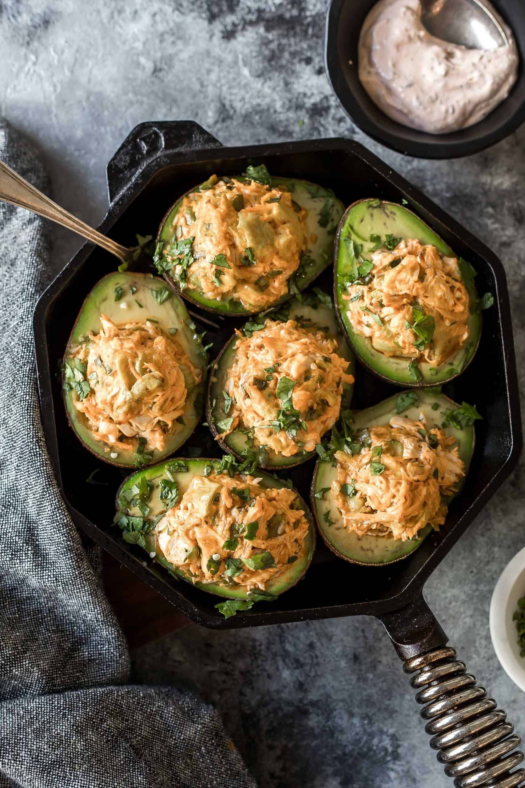 6 avocado halves filled with the cheesy buffalo chicken mixture arranged in a cast iron skillet
