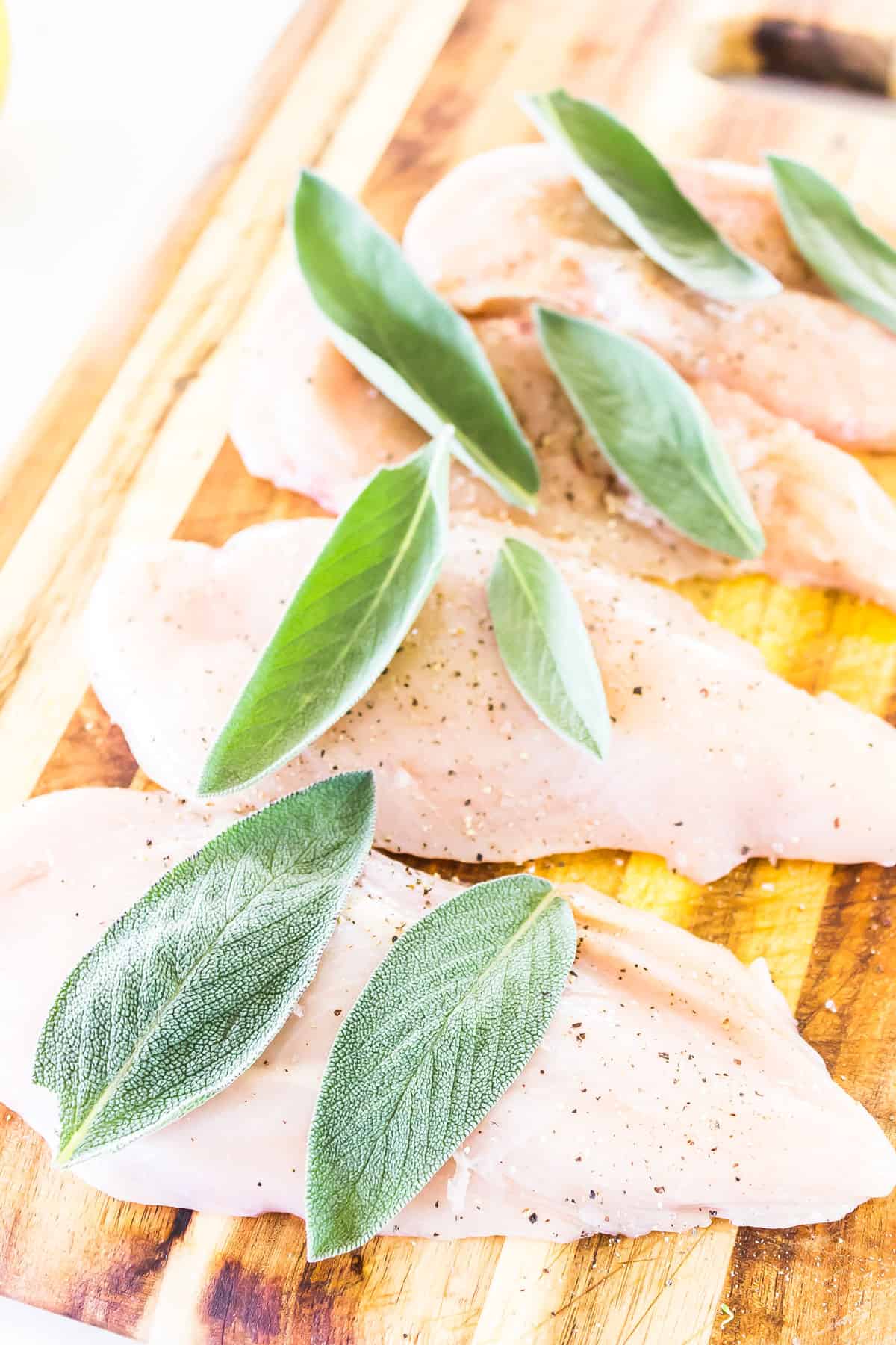 chicken breasts on a cutting board seasoned with salt and pepper and topped with sage leaves