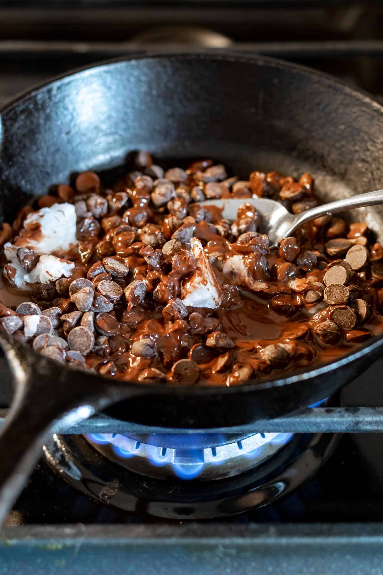 chocolate chips and coconut oil being melted in a cast iron skillet on the stovetop