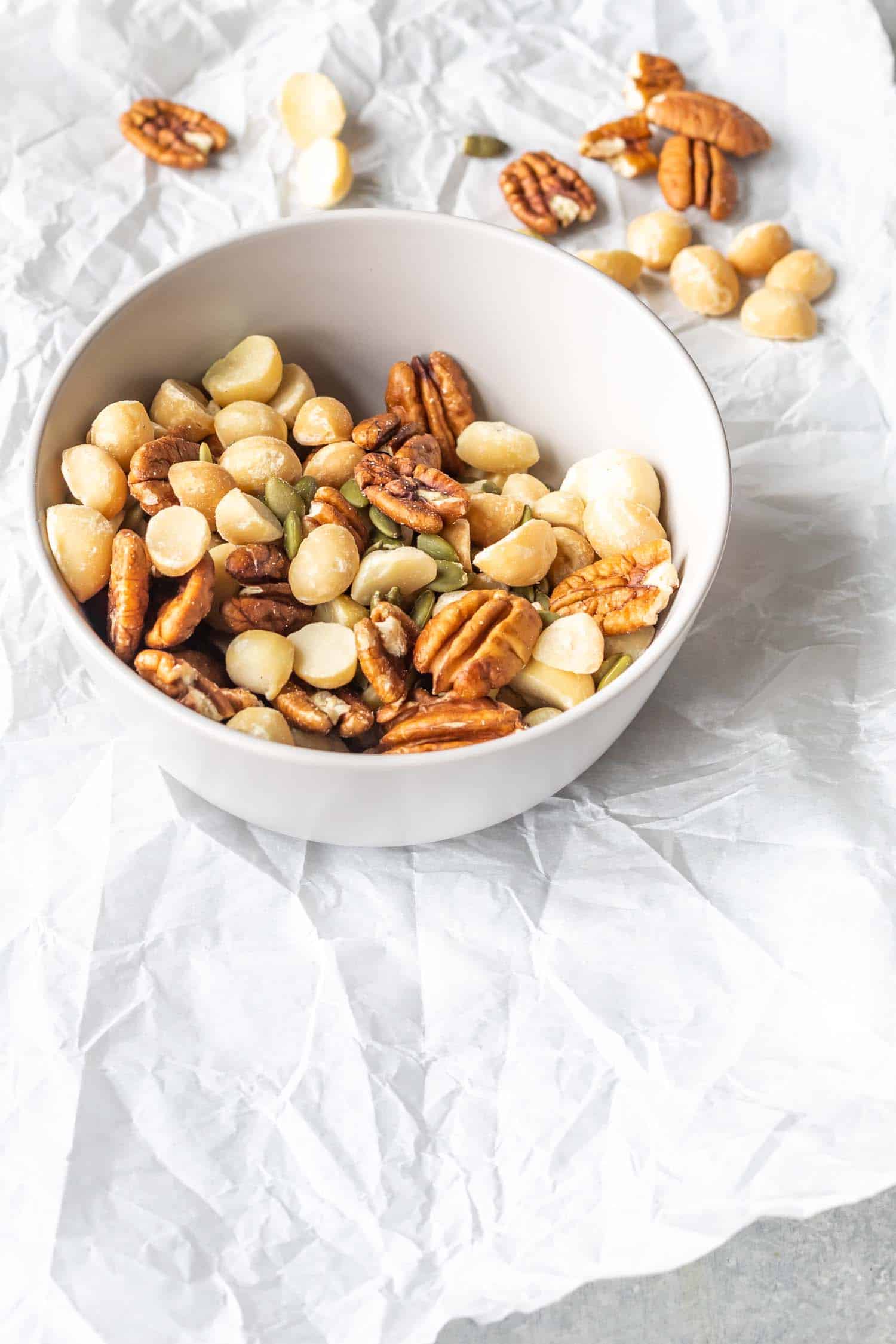 A bowl of mixed nuts and seeds on white parchment paper