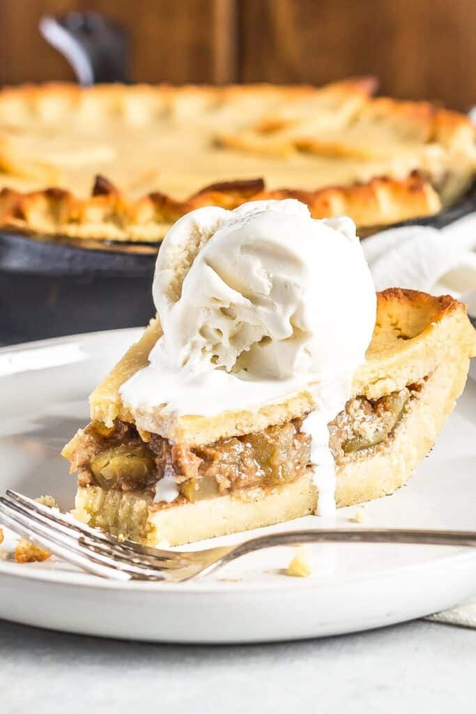 A slice of Keto Apple Pie with Ice cream on top served on a plate. Skillet in the background