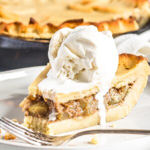 A slice of Keto Apple Pie with Ice cream on top served on a plate. Skillet in the background