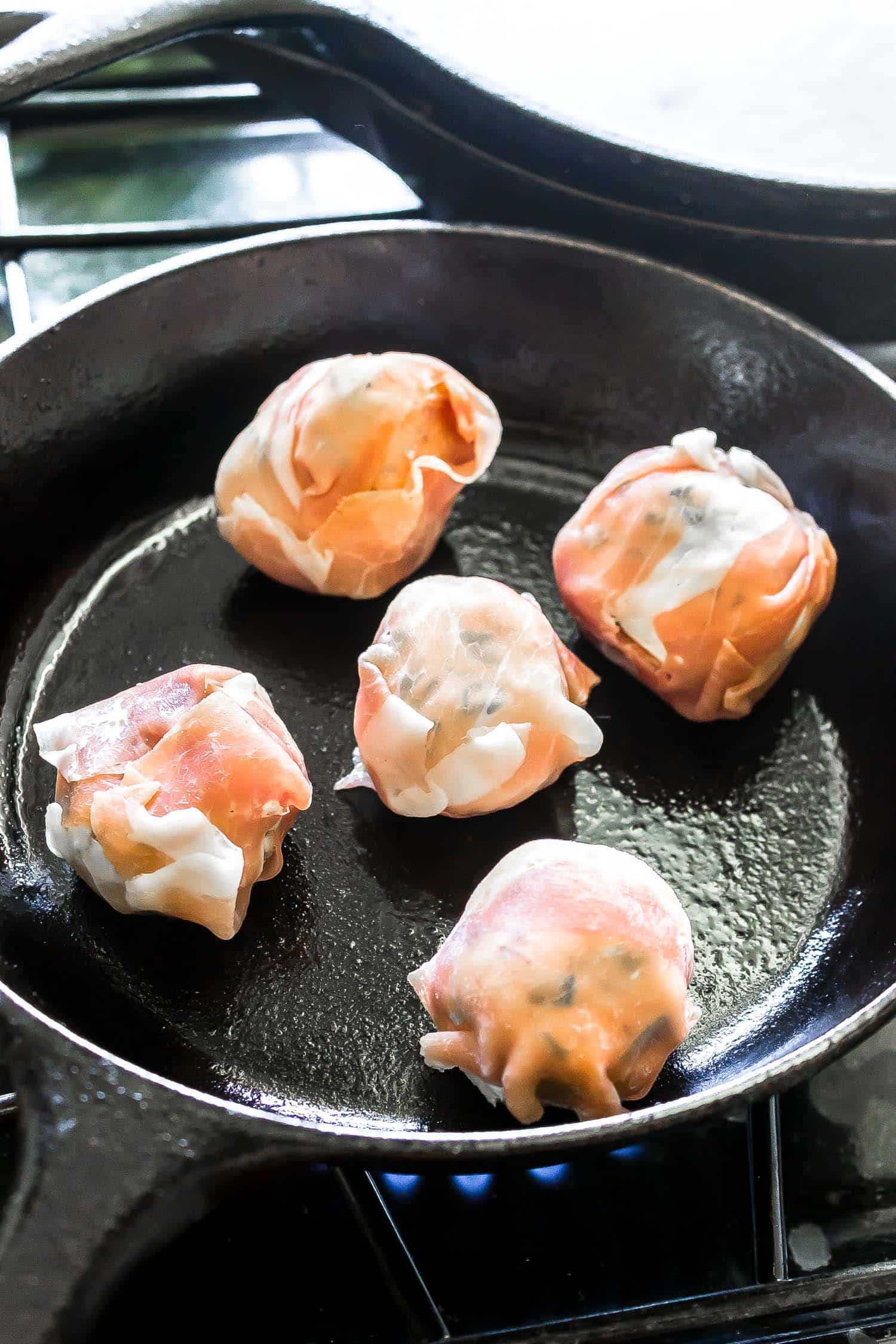fat bombs being wrapped in prosciutto and pan fried in a cast iron skillet