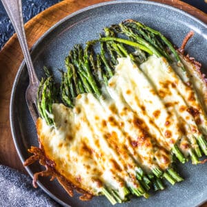 Easy Keto Cheesy Asparagus on a grey plate on a wooden charger.