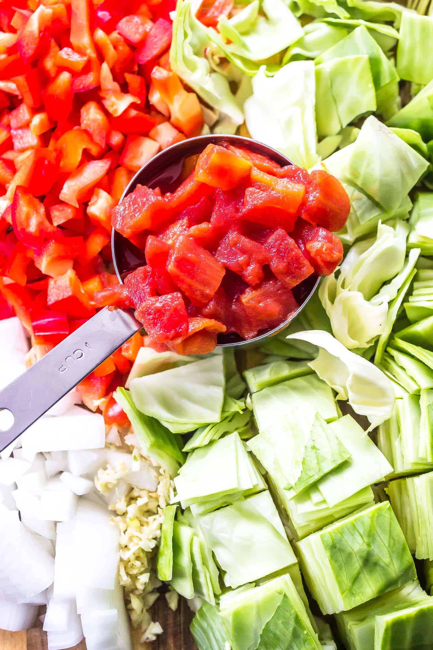 cabbage, tomatoes, bell peppers, and onions all chopped on a cutting board