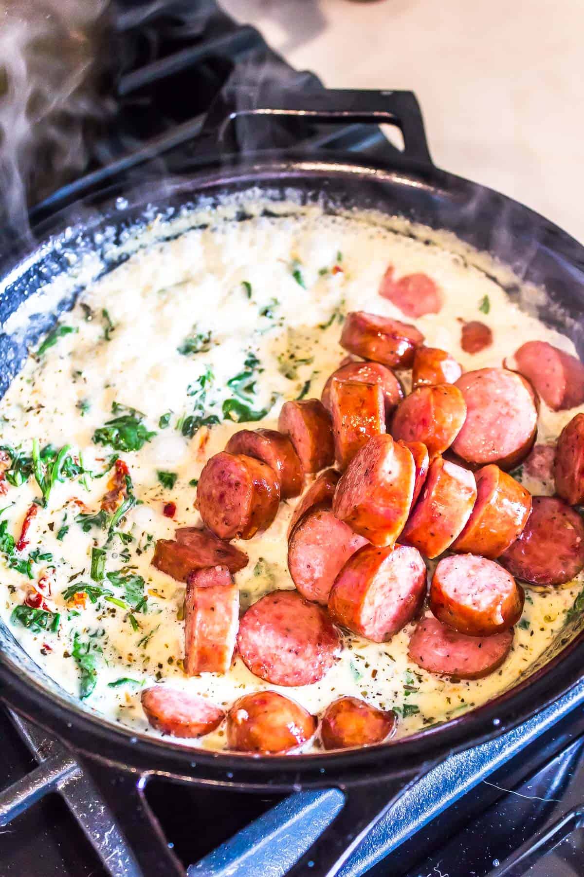 Sausage and cream sauce being mixed and beginning to be cooked