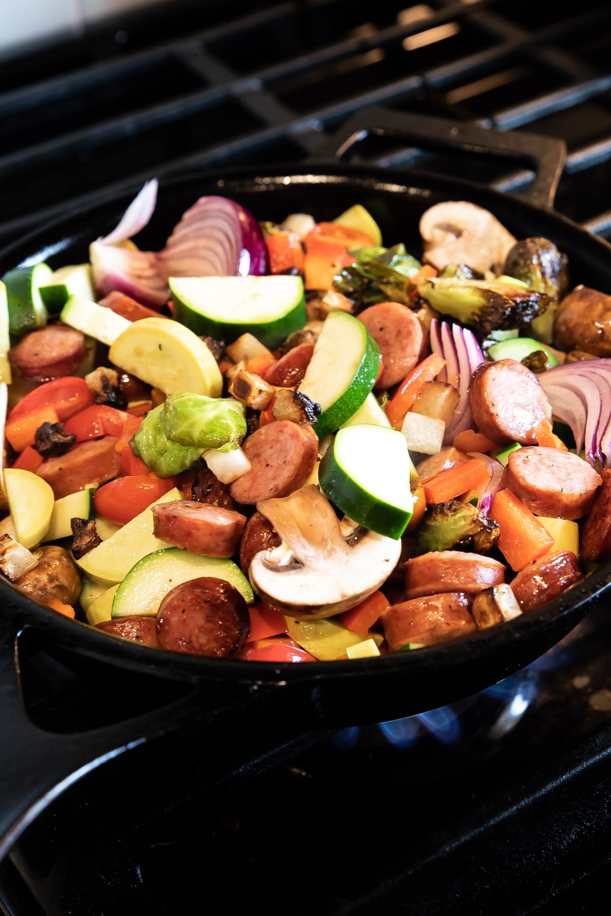 veggies piled high in a cast iron skillet over a flame from a gas range