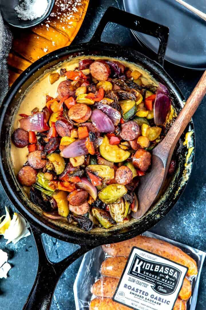 Keto Garlic Parmesan Sausage Skillet with kiolbass packaging in the foreground being stirred with a wooden spoon/