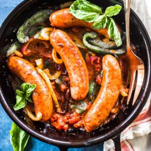 Keto Italian Sausage, Peppers, and Onions in a cast iron skillet with fresh basil.