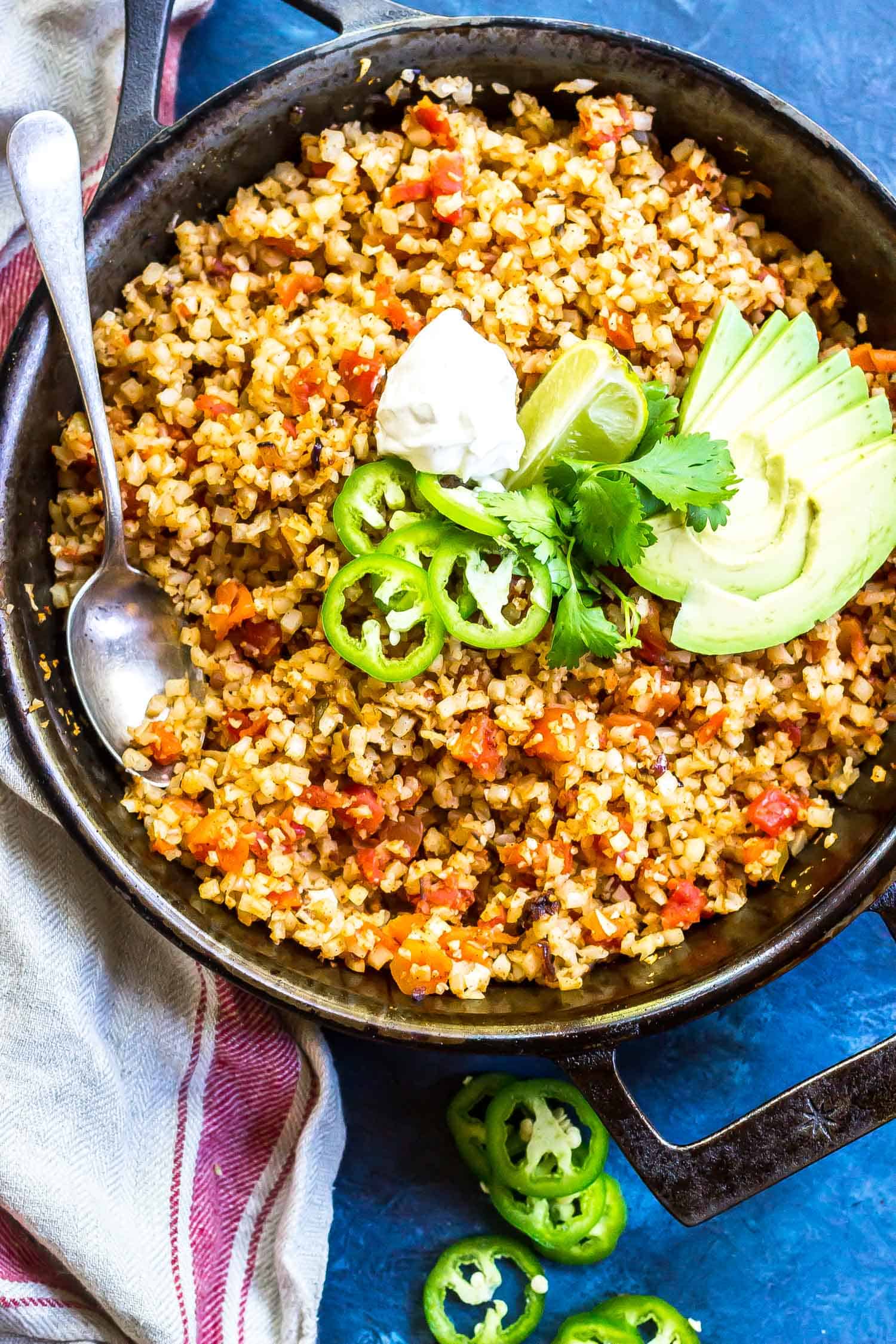 Mexican Cauliflower Rice in a cast iron skillet topped with sour cream, cilantro, avocado, and jalapenos