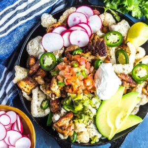 Keto Nachos in a cast iron skillet topped with salsa, avocado, sour cream, radishes, and more