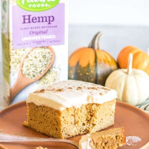 A slice of keto pumpkin spice cake on a plate in front of a carton of pacific foods unsweetened hemp beverage.