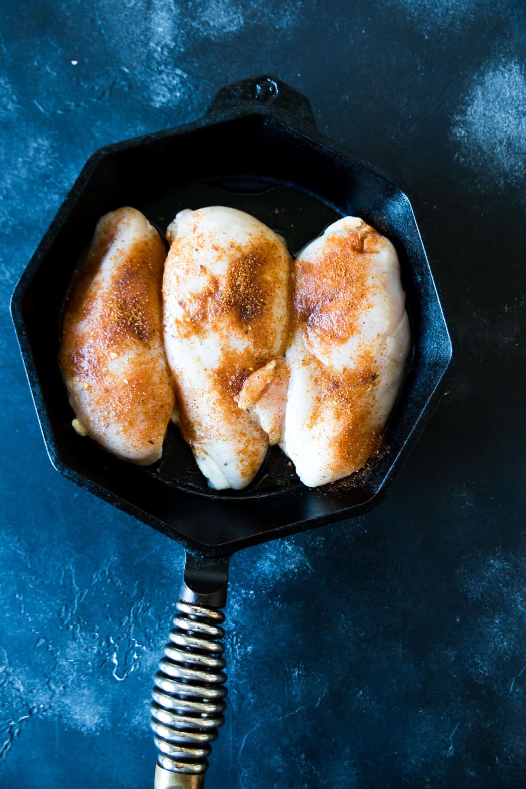 three chicken breasts, seasoned in a cast iron skillet