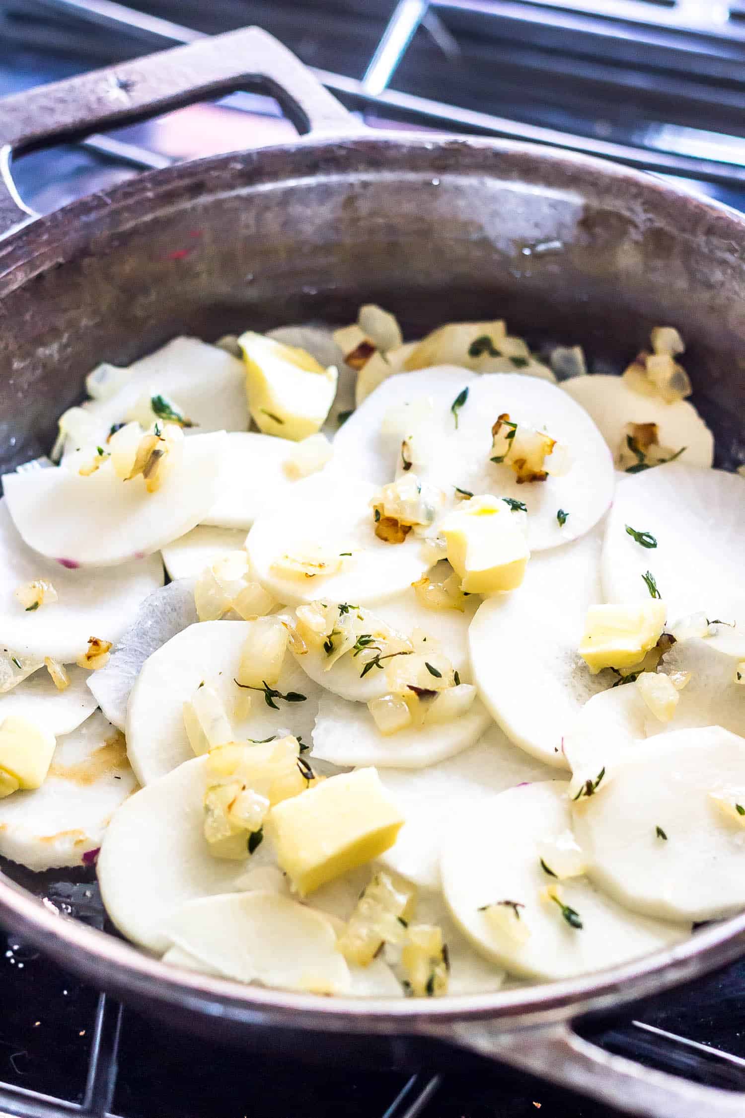 raw sliced turnips topped with sautéed herbed onions and butter in a cast iron skillet