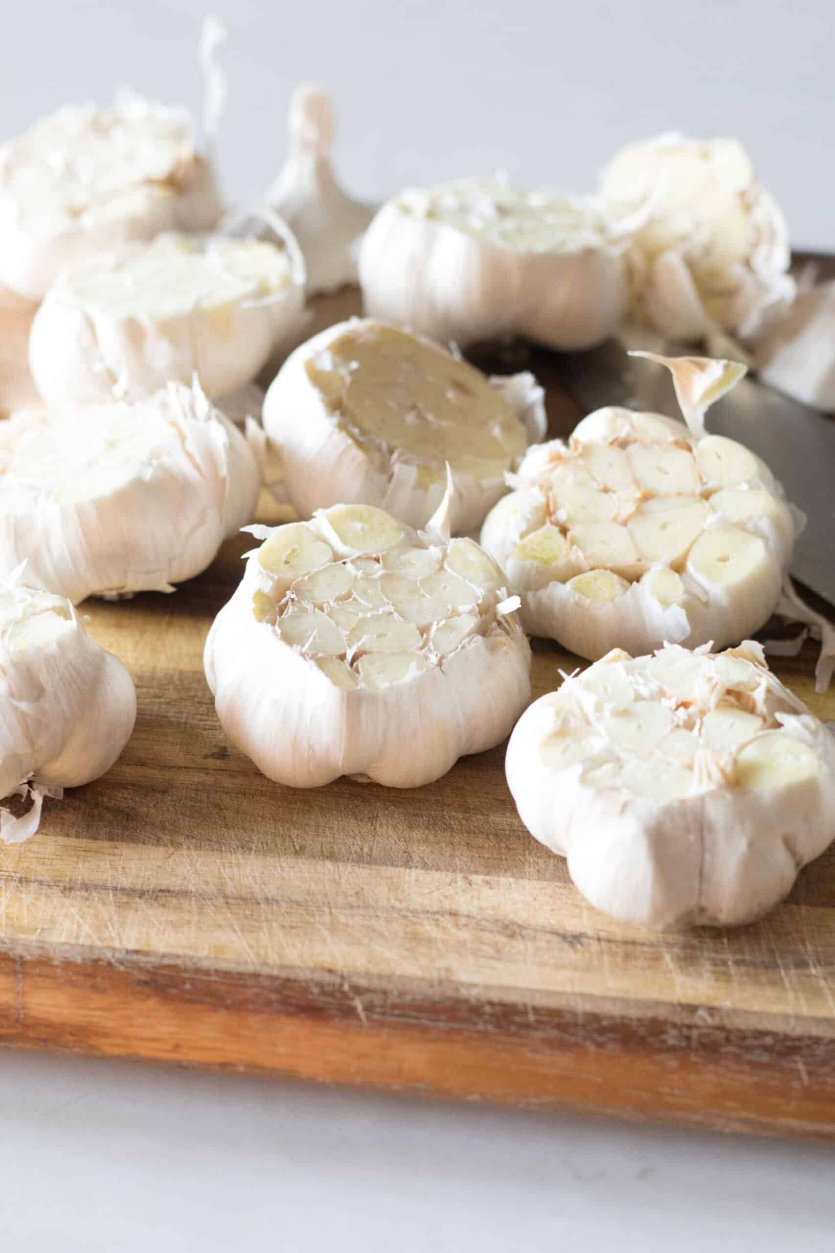 Multiple bulbs of garlic on a cutting board with the tops cut off