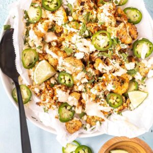 street style cauliflower on plate topped with cream, jalapenos, and lime