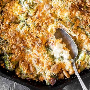 Cheesy Keto Broccoli Casserole in a cast iron skillet with a serving spoon preparing to scoop