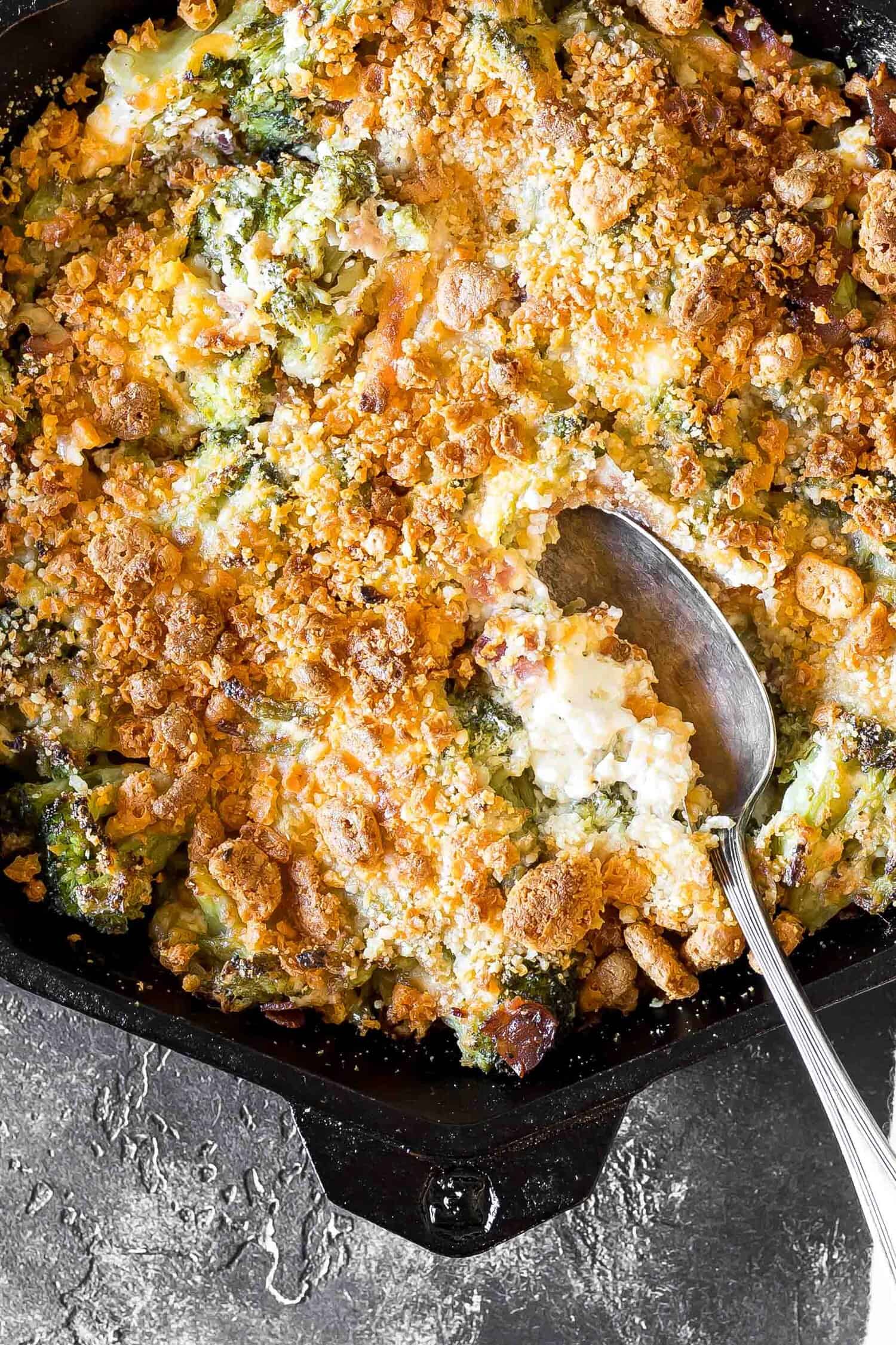 Cheesy Keto Broccoli Casserole in a cast iron skillet with a serving spoon preparing to scoop
