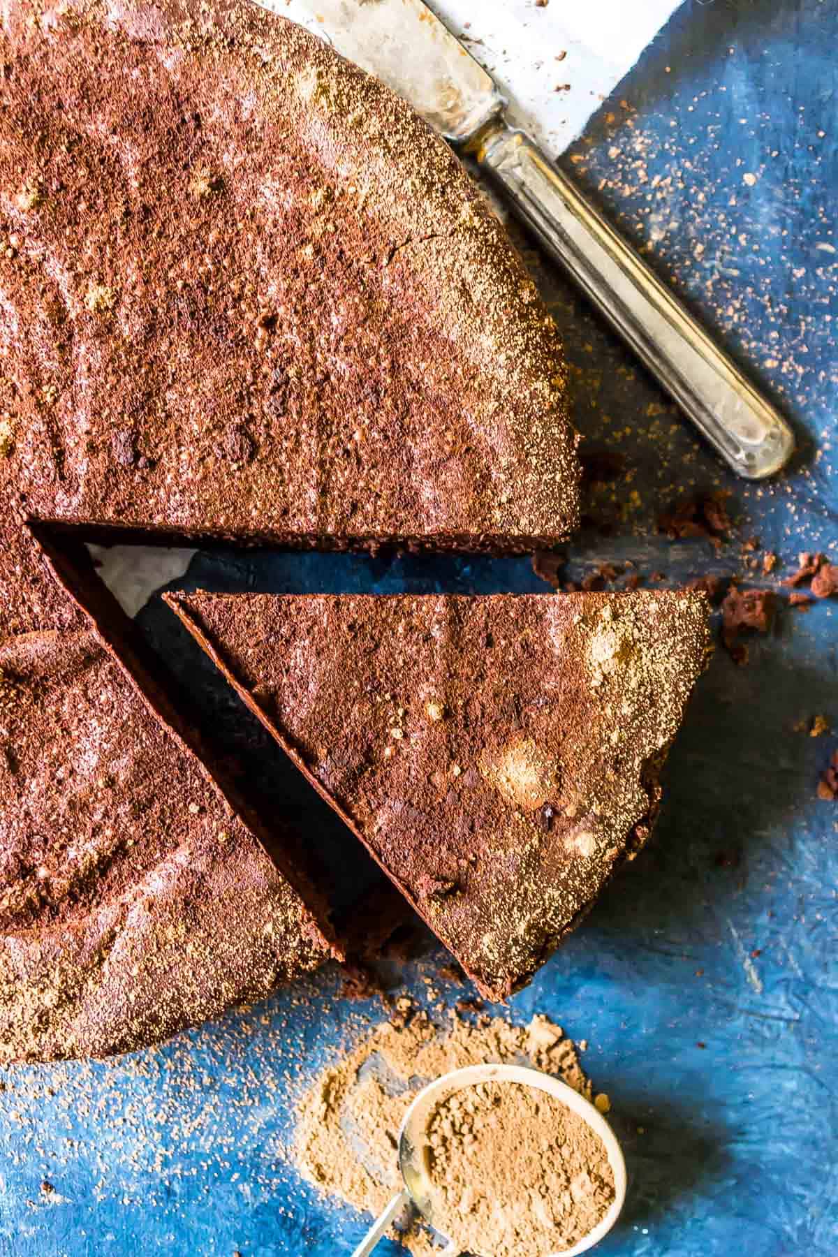 Keto Flourless Chocolate Torte on a blue background with a slice cut out with an antique knife