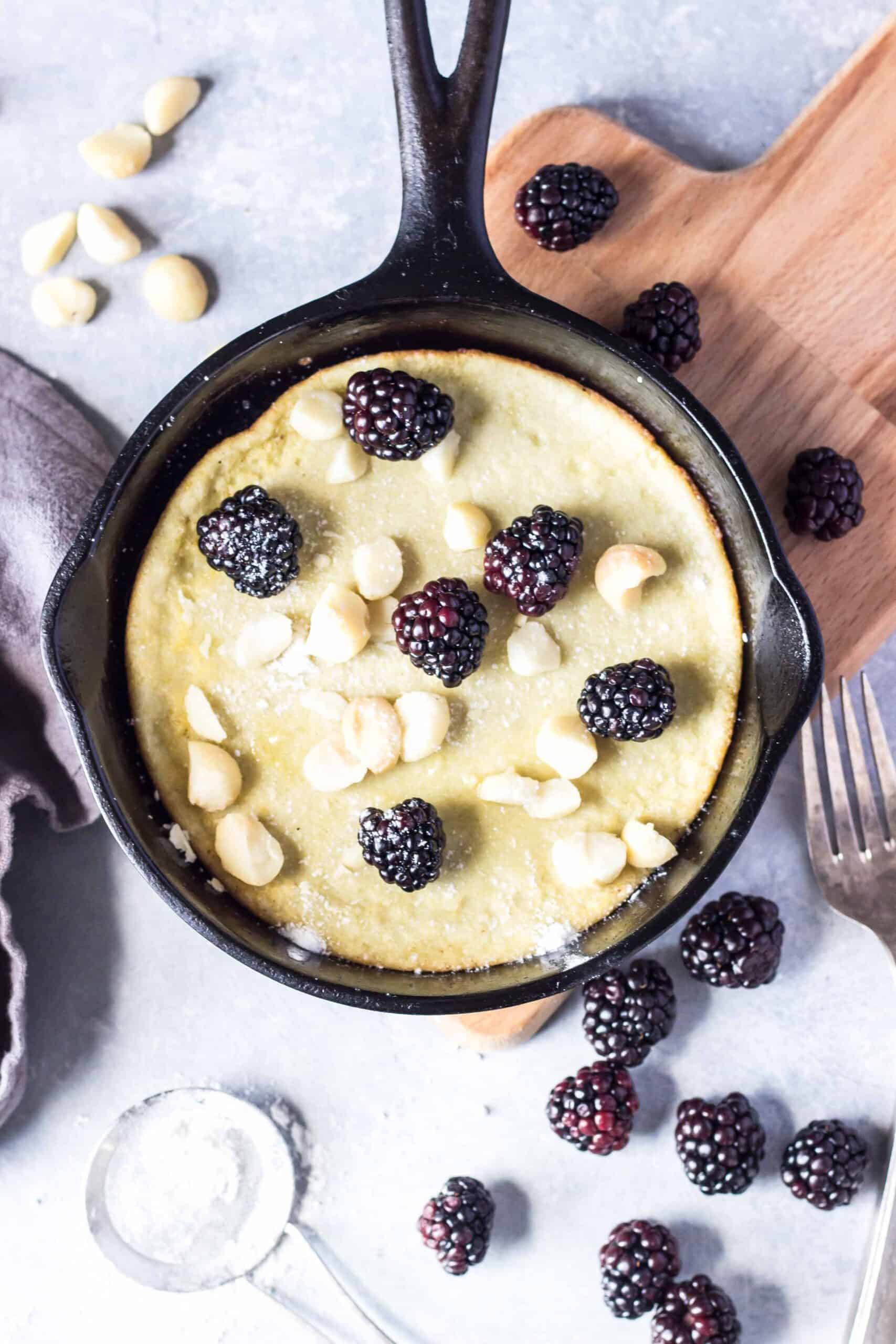 Keto Dutch Baby in a small cast iron skillet topped with blackberries and macadamia nuts