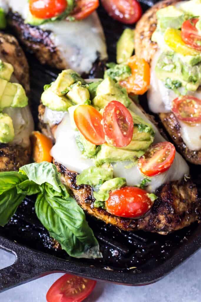Avocado Caprese Chicken in a cast iron grill pan - chicken topped with cheese, avocado, and tomatoes and basil