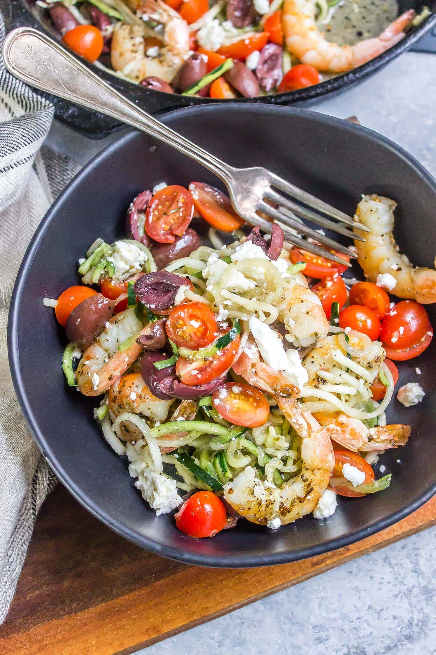 Mediterranean Keto Shrimp Zoodles in a black bowl with a grey striped tea towel to the side