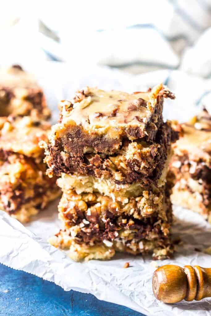 Keto Magic Bars stacked on a piece of white parchment paper on a blue background with a striped tea towel in the background