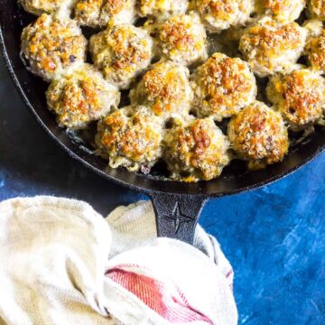 Keto Sausage Balls in a cast iron skillet on a blue background with a tea towel tied around the handle