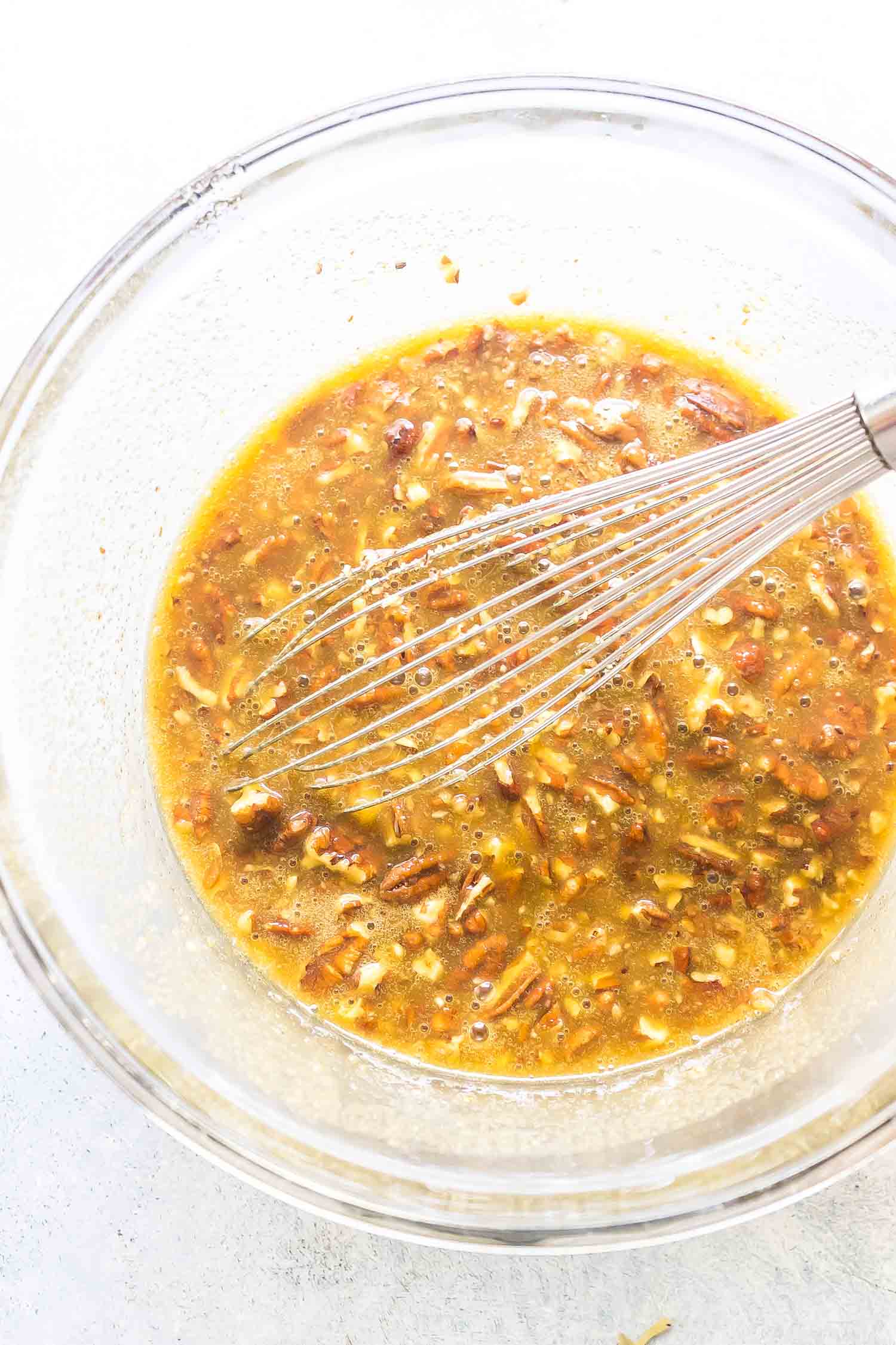 keto pecan pie filling mixture in a clear glass bowl with a whisk