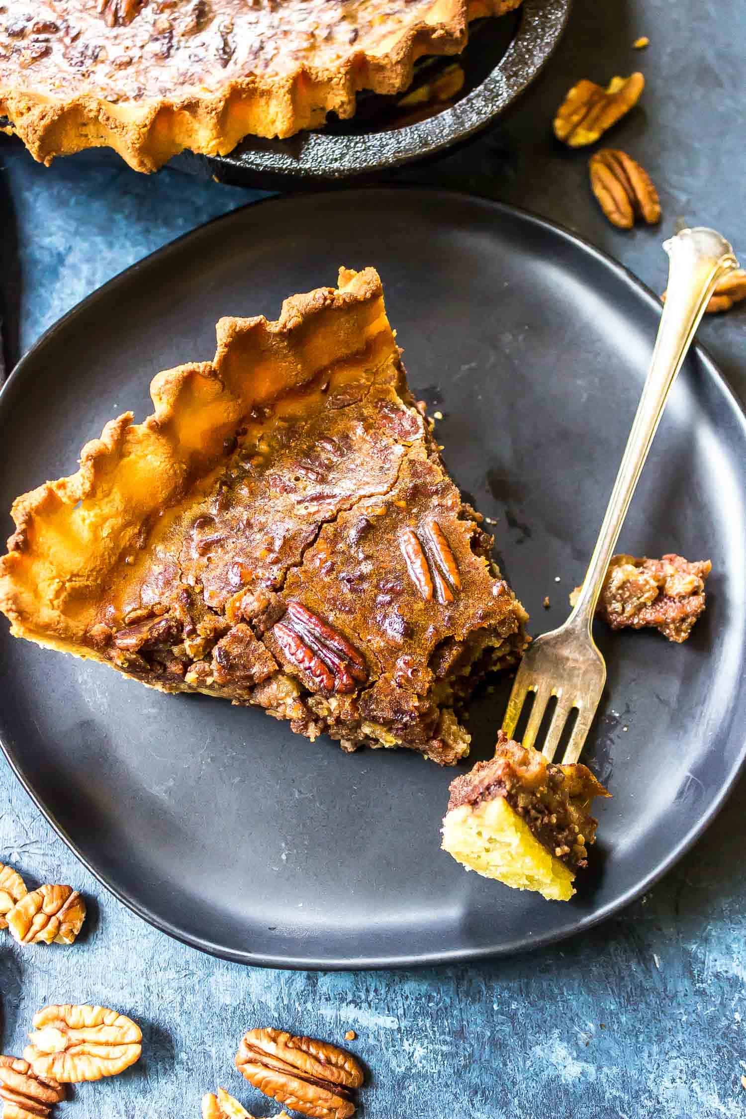 Keto Pecan Pie slice on a black plate with a fork taking a bite out of the end