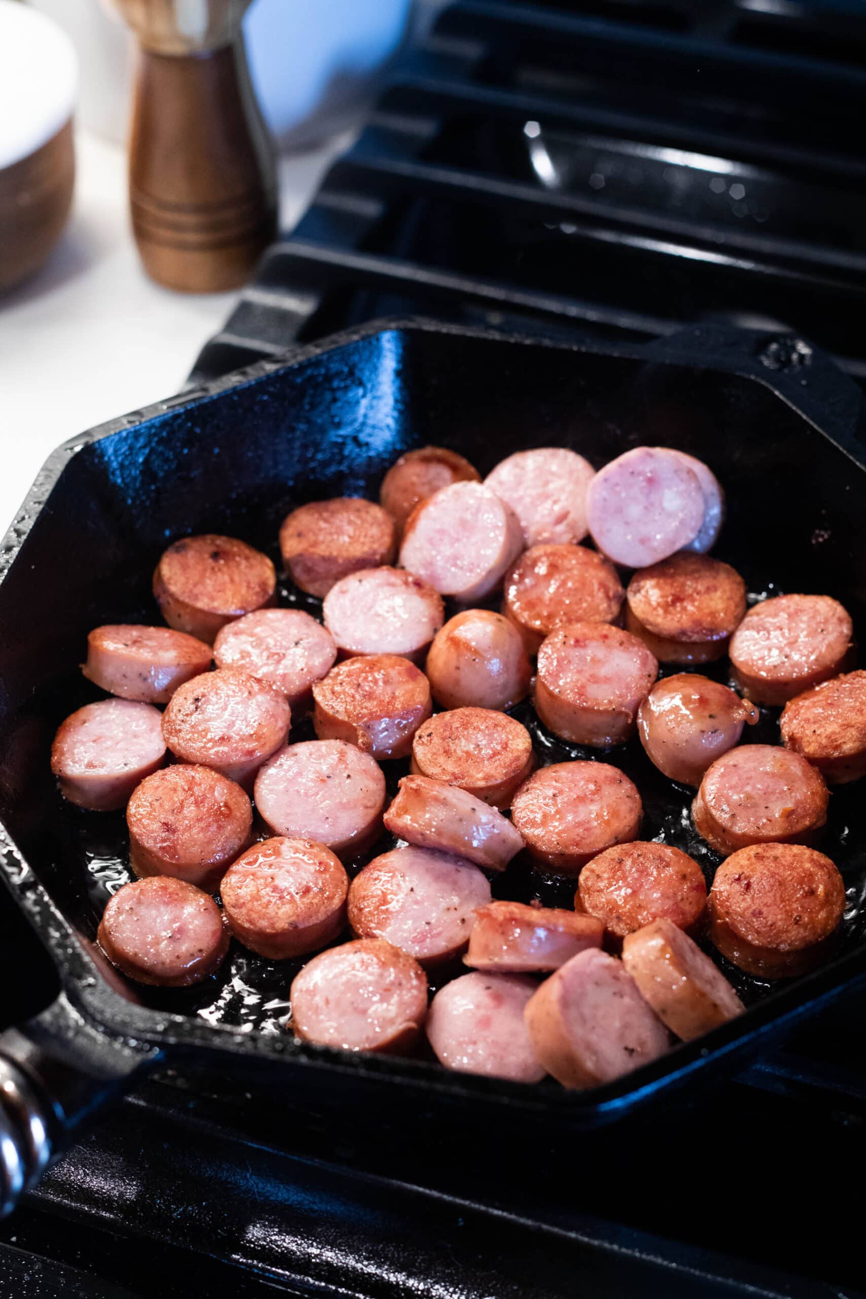 Sliced sausage rounds in a cast iron skillet atop a gas range
