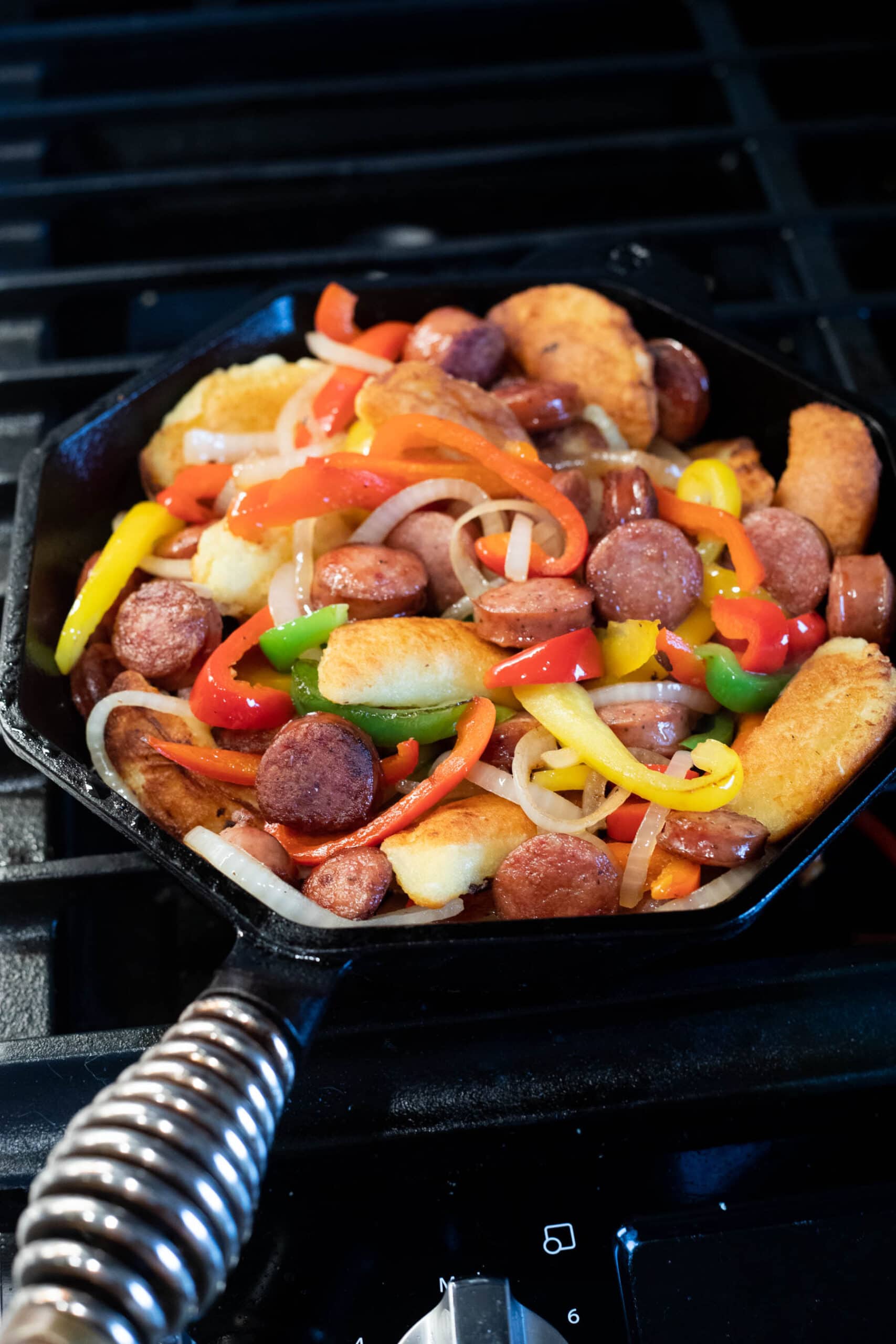 A Cast Iron Skillet filled with peppers, onions, rounds of sausage and keto pierogi's in the process of cooking.