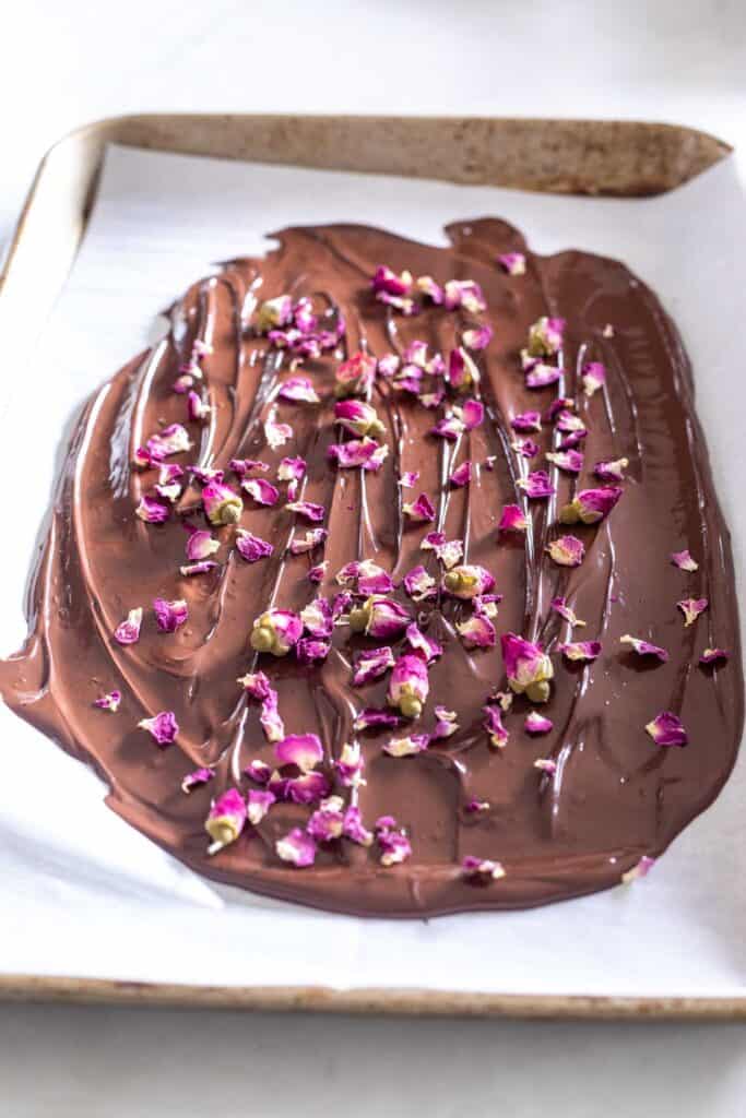 melted chocolate on parchment lined baking sheet topped with edible rose petals