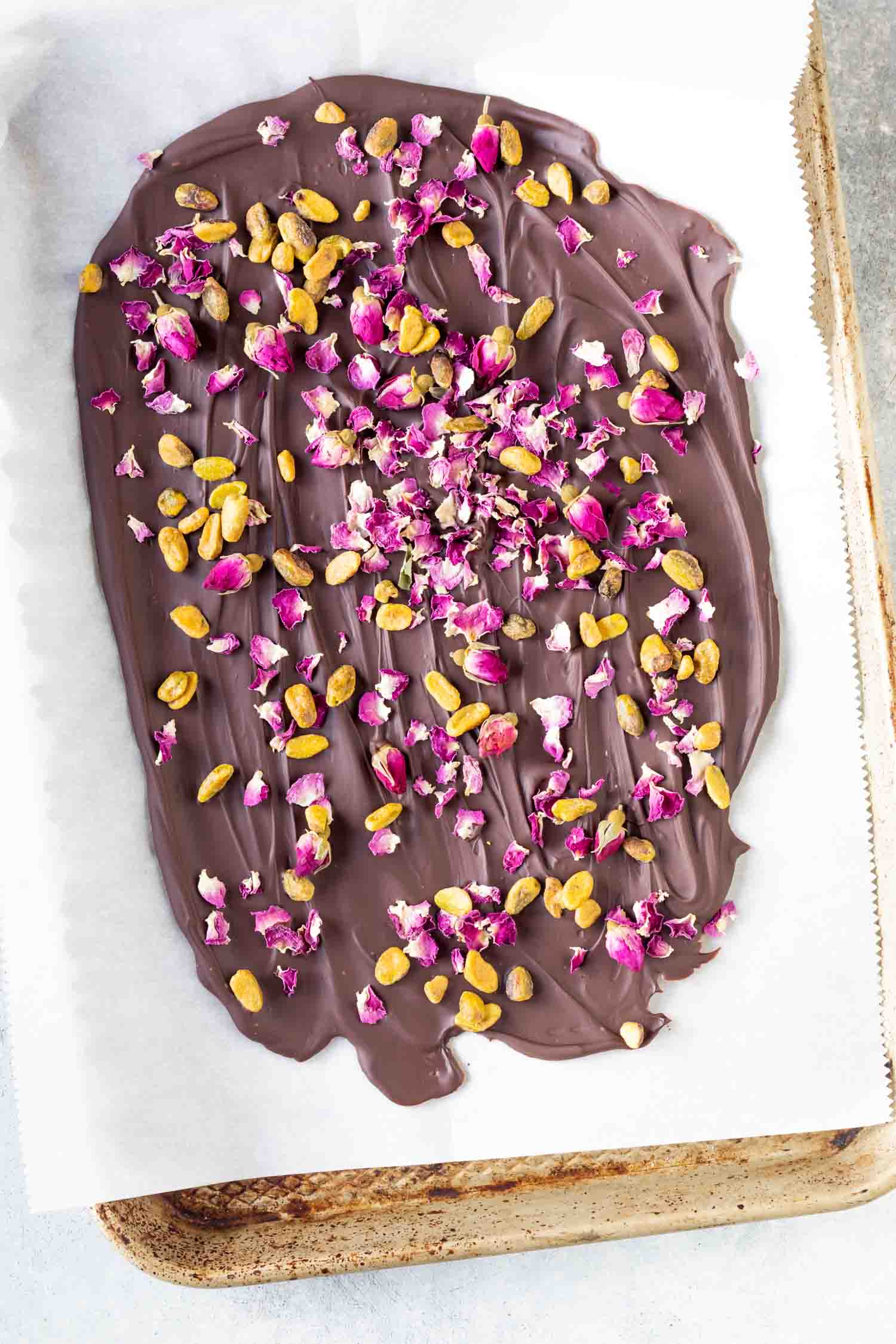 melted chocolate on parchment lined baking sheet topped with edible rose petals and pistachios