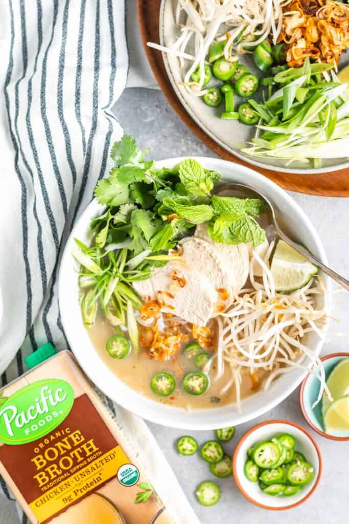 Keto Vietnamese Chicken Noodle Soup in bowl with a plate of toppings to the side